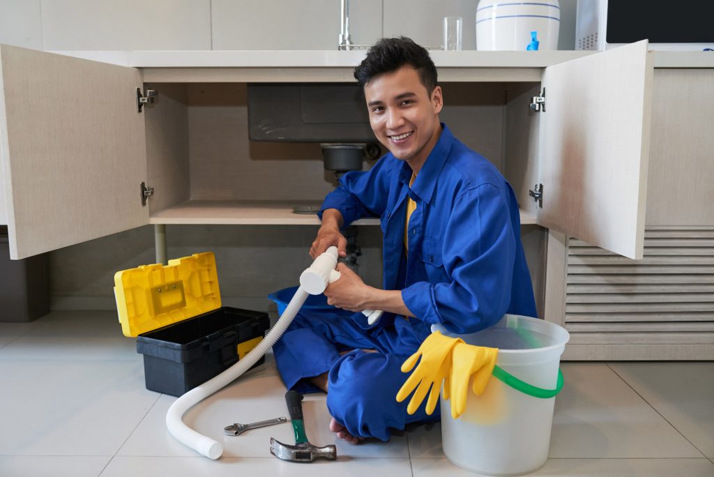 Plumber with a drain snake clearing a clogged drain under a sink