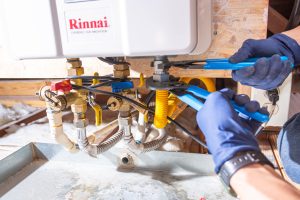 Plumber tightening fittings under a Rinnai tankless water heater