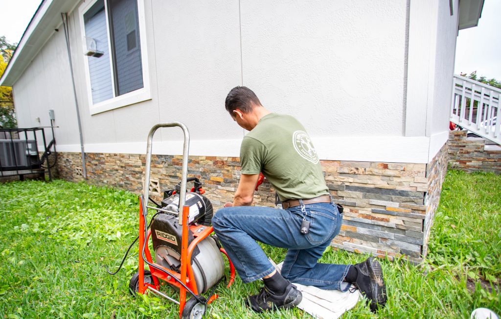 H-Town Plumbers plumber operating a sewer drain cleaning machine in a backyard