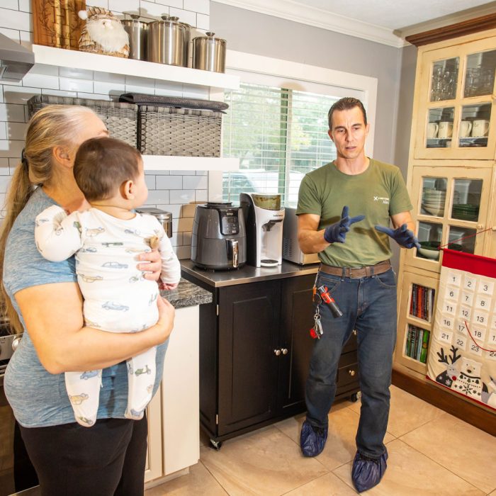 H-Town Plumbers plumber talking with a homeowner holding a baby in a Houston kitchen