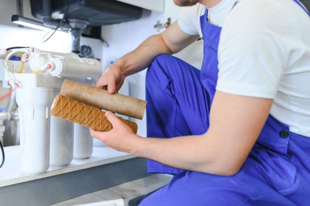 Plumber replacing a water filter cartridge under a sink